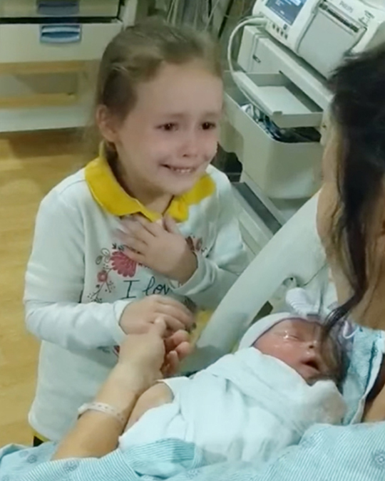 As soon as the little girl sees her newborn sister for the first time in her mother's arms, she begins to cry with joy.